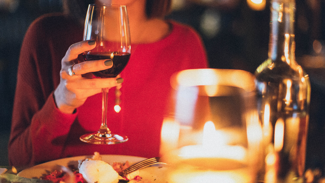 gedeckter Tisch und eine Dame mit Weinglas in der Hand bei einem romantischen Dinner